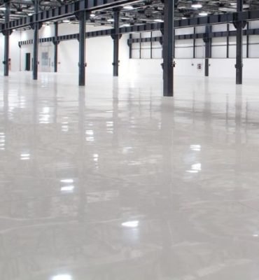 High-gloss resin rich floors with bright white commercial epoxy flooring inside a large open industrial-style building.